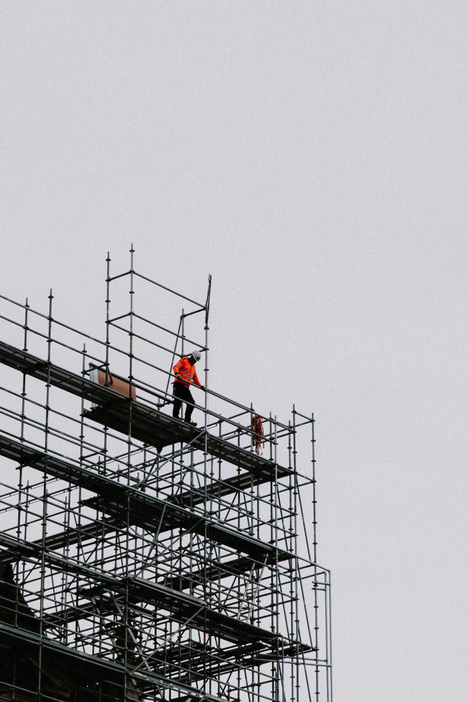 A worker in high-visibility clothing on scaffolding high on a building under construction